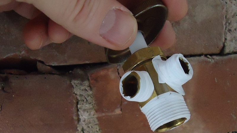 Hand holding a brass shutoff valve wrapped in white thread tape, a plumbing service repair for a burst pipe