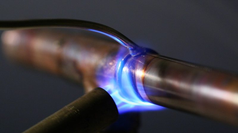 Plumber soldering a copper pipe joint with a propane torch during a burst pipe repair