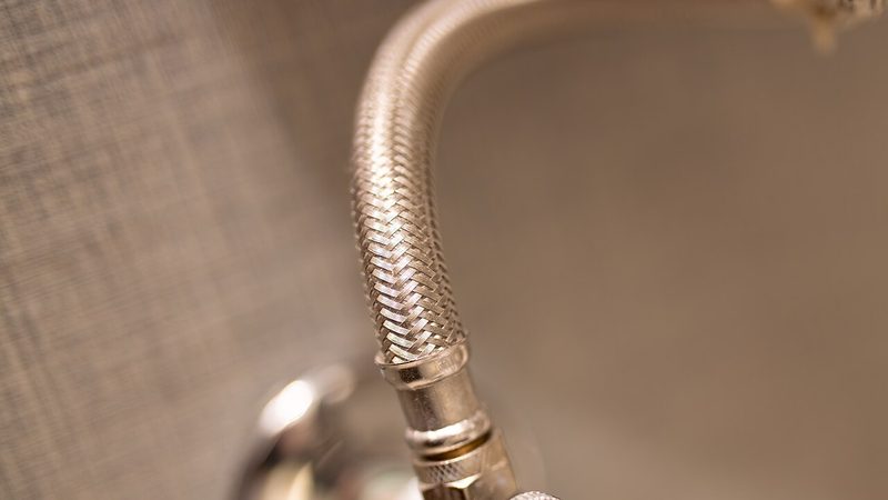 Close-up of a braided stainless steel supply pipe and shutoff valve, the kind of fixture line behind a burst supply pipe leak