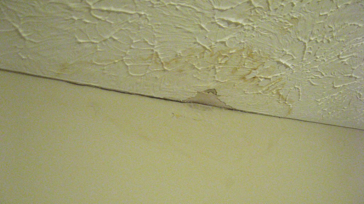 Brown water stain and cracked drywall on a home ceiling where a pipe leak has soaked through, the kind of interior damage a burst pipe can cause