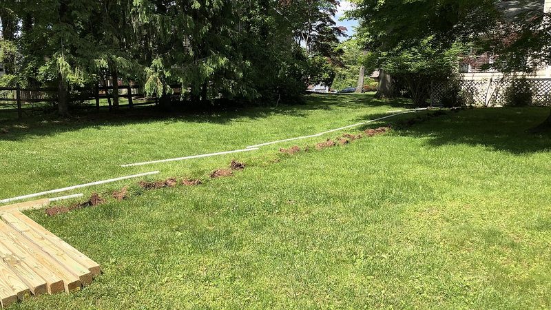 A white pipe laid along a shallow trench dug across a home's back lawn for an underground water pipe repair