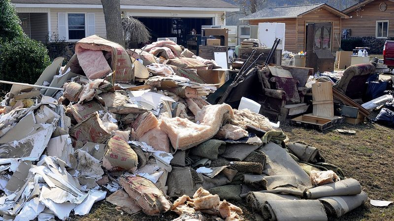 Water-damaged insulation, drywall, and carpet pulled out during frozen pipe damage cleanup and stacked on the front lawn for disposal