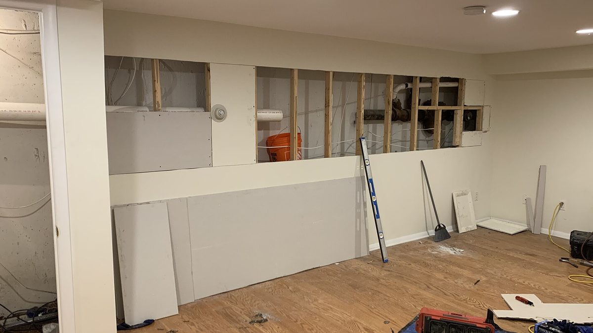 Open basement wall during a renovation showing exposed framing and plumbing pipe behind the drywall, the kind of access needed to fix a broken pipe under the house