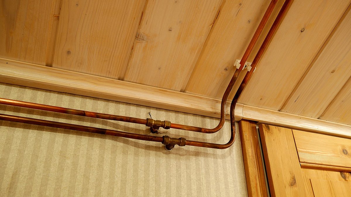 Copper main water pipe and brass fittings running along a home wall under a wooden ceiling