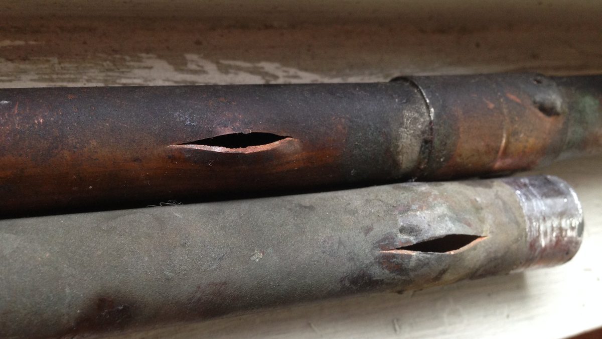 Two copper water pipes with split holes in them, lying on an interior shelf, showing a burst pipe