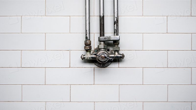 A shutoff valve and pipes mounted on a tiled bathroom wall, the kind of fitting that can hiss or drip when a pipe bursts