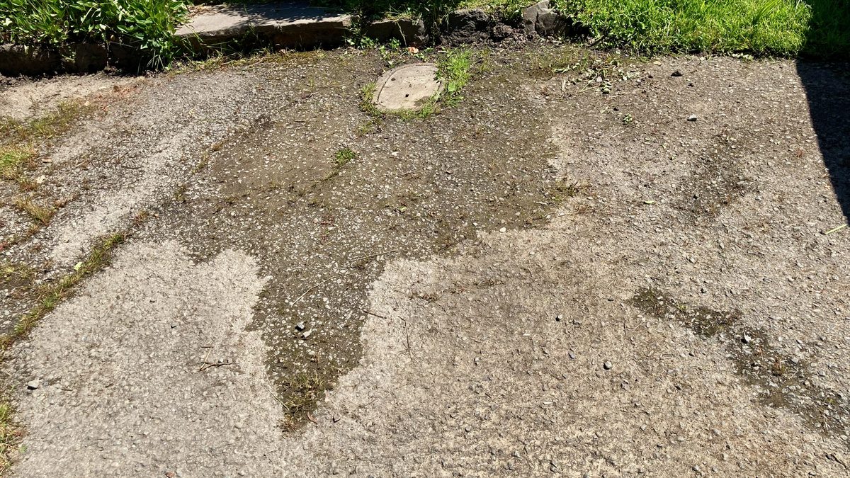 Wet patch from a burst pipe under a cracked concrete driveway near a buried water meter lid
