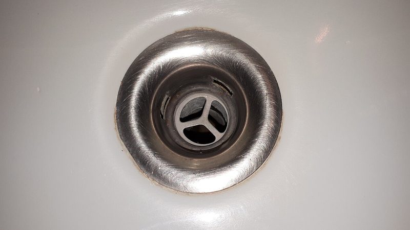 Close-up of a bathroom sink drain with a brushed steel strainer in a white basin, the spot where a clogged drain starts