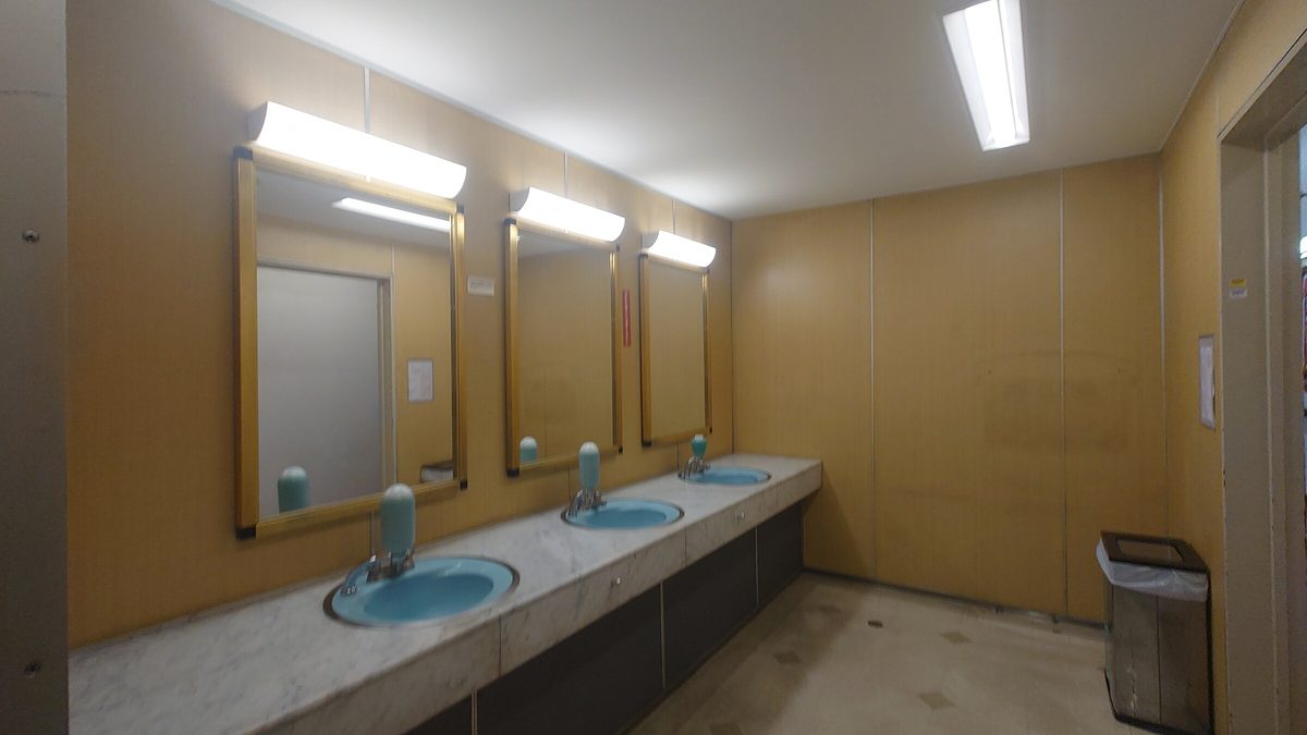 Bright workplace restroom with three sinks, mirrors and a tiled floor, where a toilet overflow needs quick cleanup