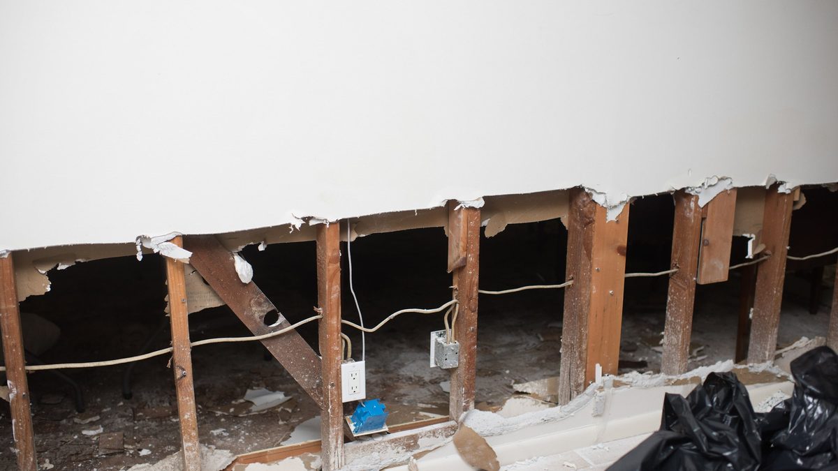 Interior wall cut open to the studs after water damage, exposing framing and an outlet behind a leaking wall