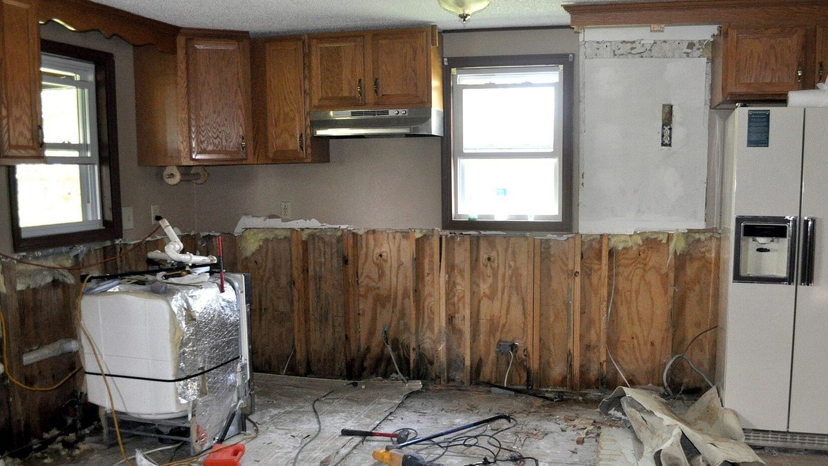 Kitchen mid water damage restoration, with wet drywall cut away, exposed studs, and repair tools on the floor