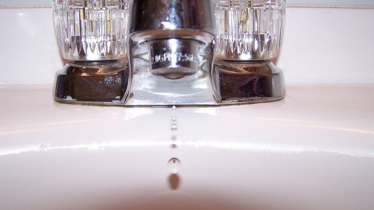 Water dripping from a bathroom faucet onto a white sink, an active leak in a house that needs to be traced to its source