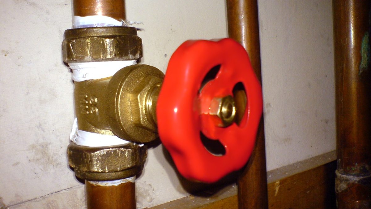 Red-handled gate valve on a copper pipe, the main shutoff valve to close first when a pipe bursts